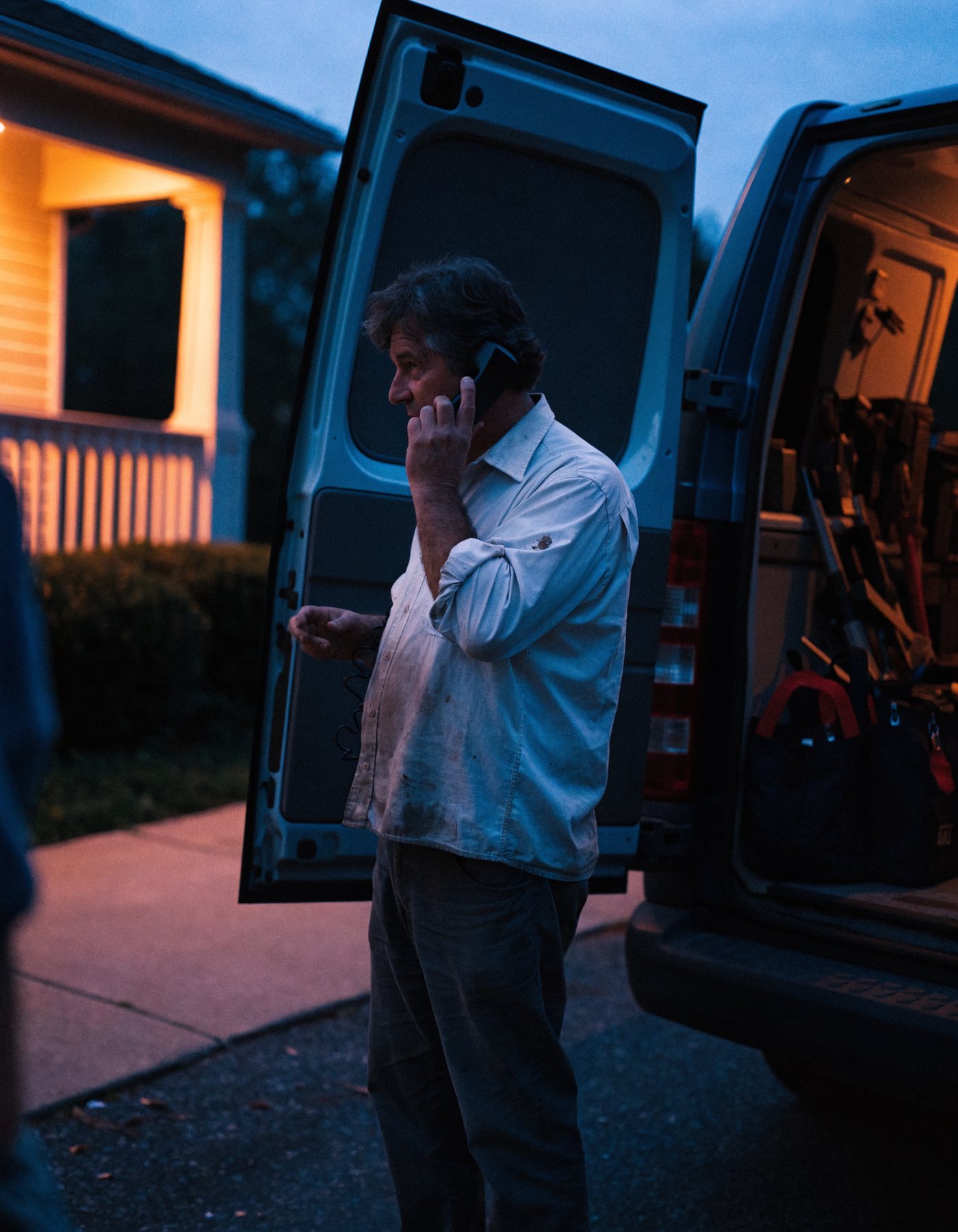 A repair business owner taking a call beside his open service van at dusk